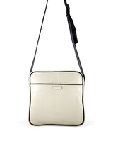 Square medium cross body bag. Cream colored leather with black leather accent stripe on front panel and black piping. Lightweight black cotton lining. Silver buckle on adjustable black leather cross body strap. Slip pocket on back panel. Upcycled, circular, sustainable. Back view.