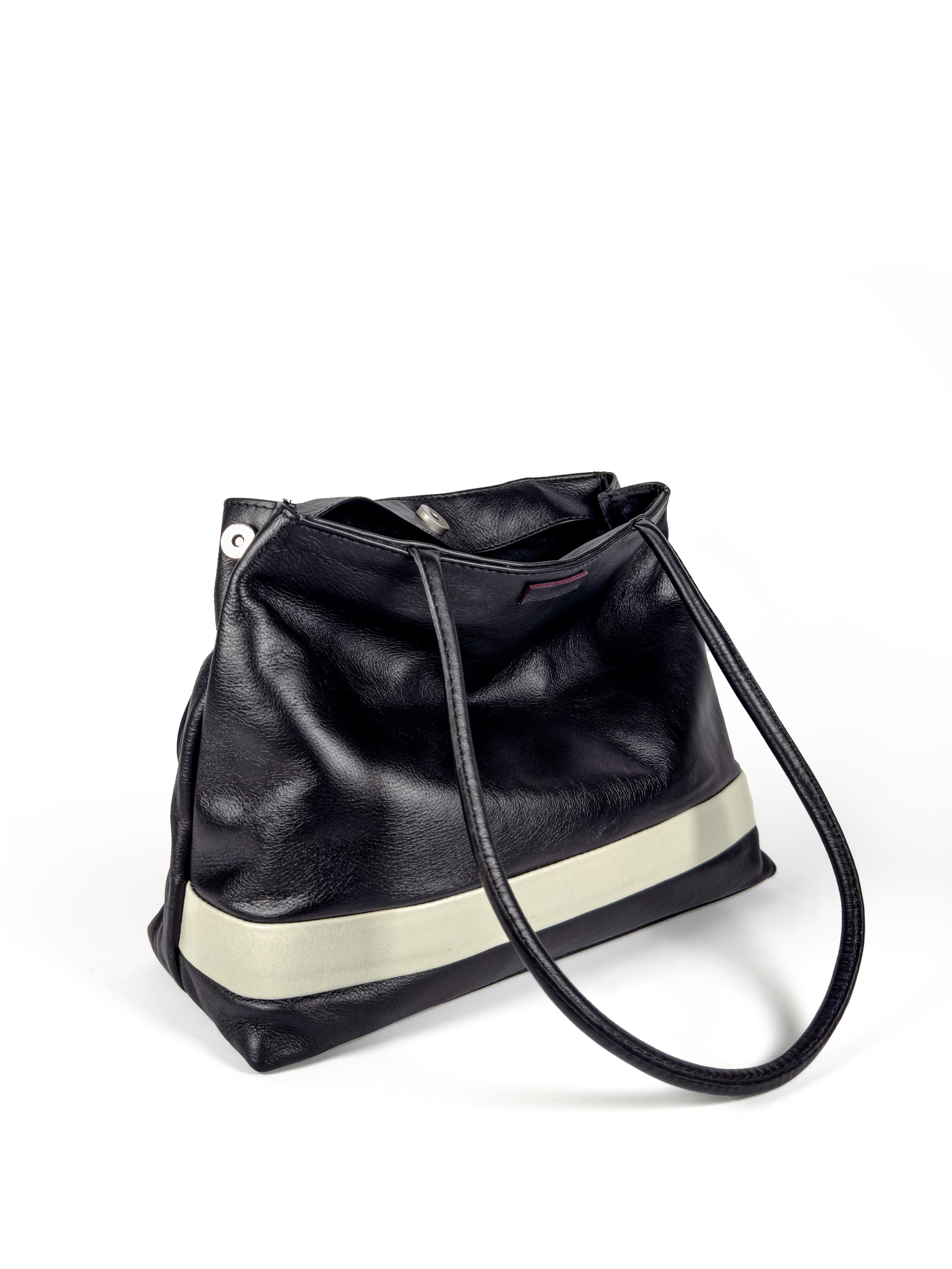 Black leather medium sized handbag, with tapered top. Inlaid white leather accent stripe on front panel. Magnet depth expansion. Chic padded pipe shoulder straps. Upcycled, circular, sustainable. 3/4 view 2.