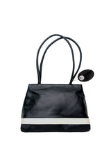 Black leather medium sized handbag, with tapered top. Inlaid white leather accent stripe on front panel. Magnet depth expansion. Chic padded pipe shoulder straps. Upcycled, circular, sustainable. Front view.