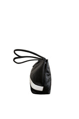 Black leather medium sized handbag, with tapered top. Inlaid white leather accent stripe on front panel. Magnet depth expansion. Chic padded pipe shoulder straps. Upcycled, circular, sustainable. Side view.