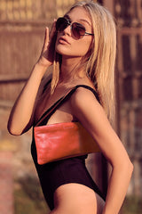 Model wearing small slim vivid orange leather handbag. Playful pale orange satin lining and contrast stitch accent. Sunken zipper closure. Upcycled, circular, sustainable.