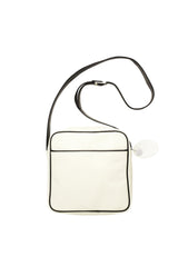 Square medium cross body bag. Cream colored leather with black leather accent stripe on front panel and black piping. Lightweight black cotton lining. Silver buckle on adjustable black leather cross body strap. Slip pocket on back panel. Upcycled, circular, sustainable. Back view.