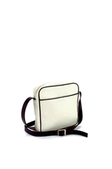 Square medium cross body bag. Cream colored leather with black leather accent stripe on front panel and black piping. Lightweight black cotton lining. Silver buckle on adjustable black leather cross body strap. Slip pocket on back panel. Upcycled, circular, sustainable. 3/4 back view.