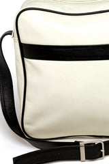 Square medium cross body bag. Cream colored leather with black leather accent stripe on front panel and black piping. Lightweight black cotton lining. Silver buckle on adjustable black leather cross body strap. Slip pocket on back panel. Upcycled, circular, sustainable. Detail view.