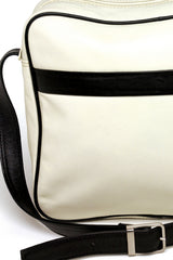 Detail view: Square medium cross body bag, off white zip closure, off white leather with inlaid black leather stripe on front panel, black piping. Black leather adjustable cross body strap with silver buckle. Back exterior slip pocket
