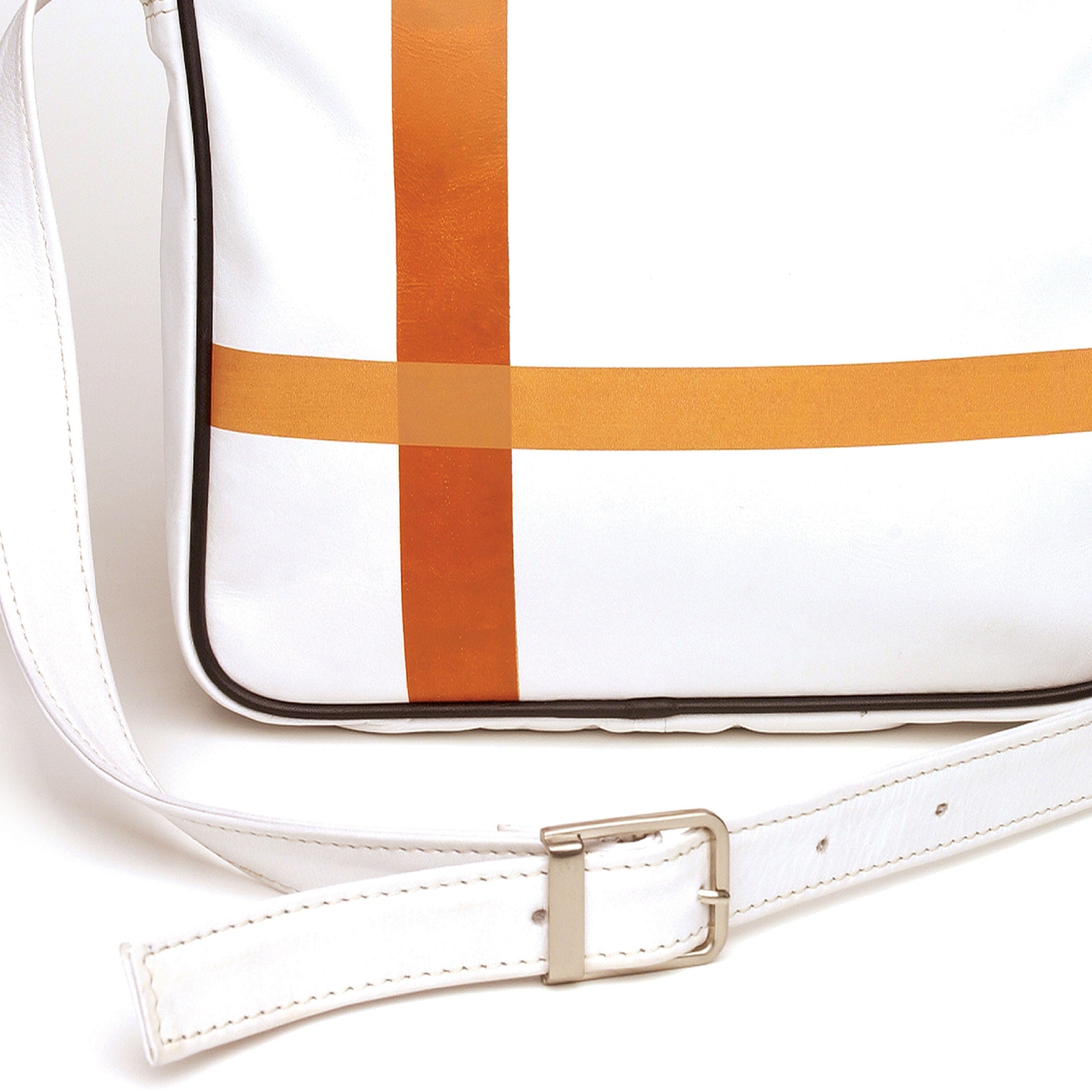 Detail view: Square medium cross body bag, white coil zip closure, all white lightly distressed leather with two toned orange silkscreen off-center cross, black piping. Silver buckle on adjustable cross body strap. Upcycled, sustainable.